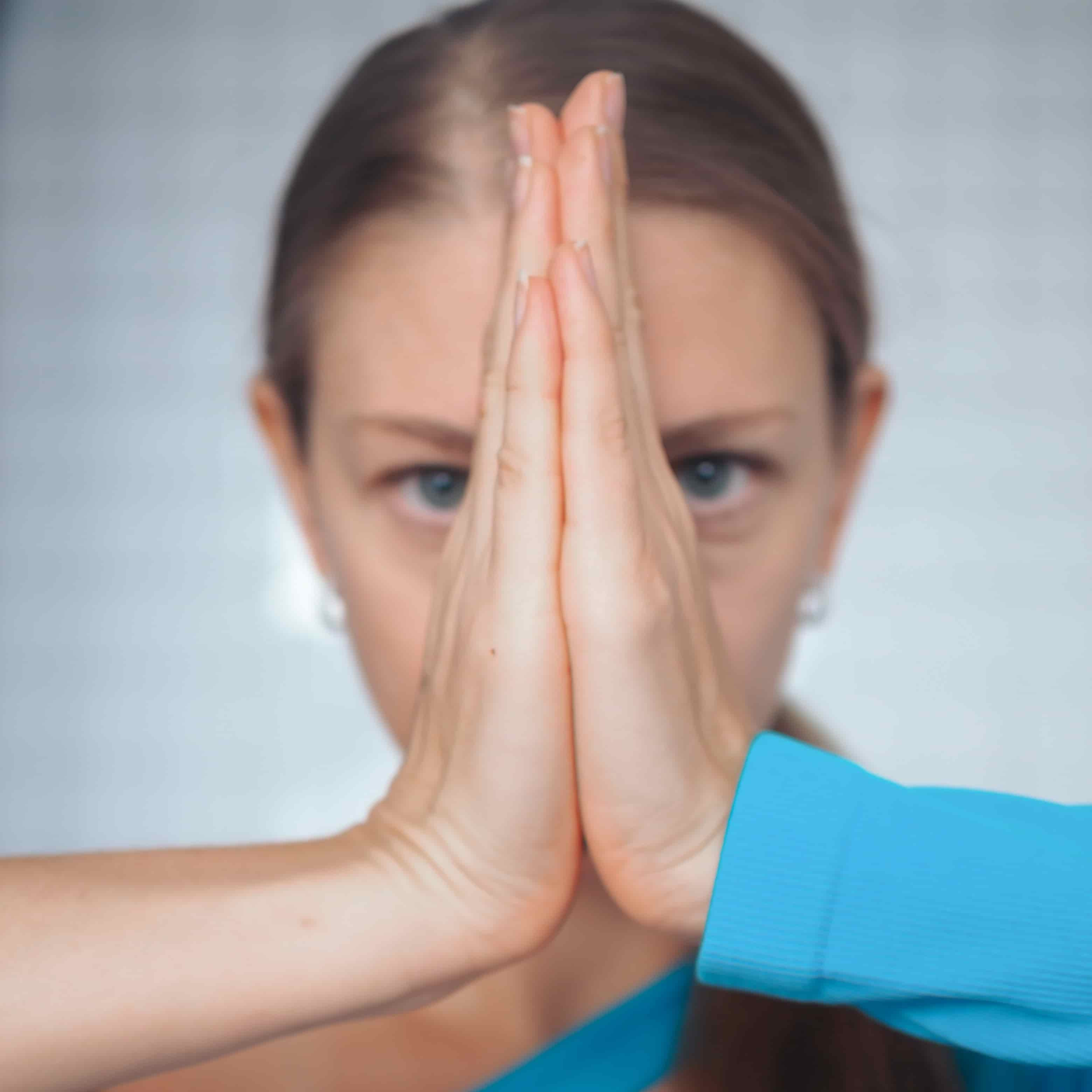 une femme qui joint ses deux mains devant son visage