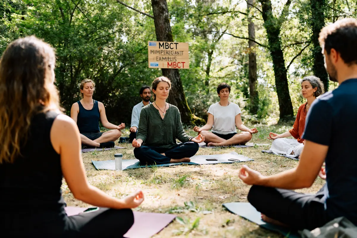 Personnes méditant en cercle dans la forêt pendant la formation MBCT en plein air